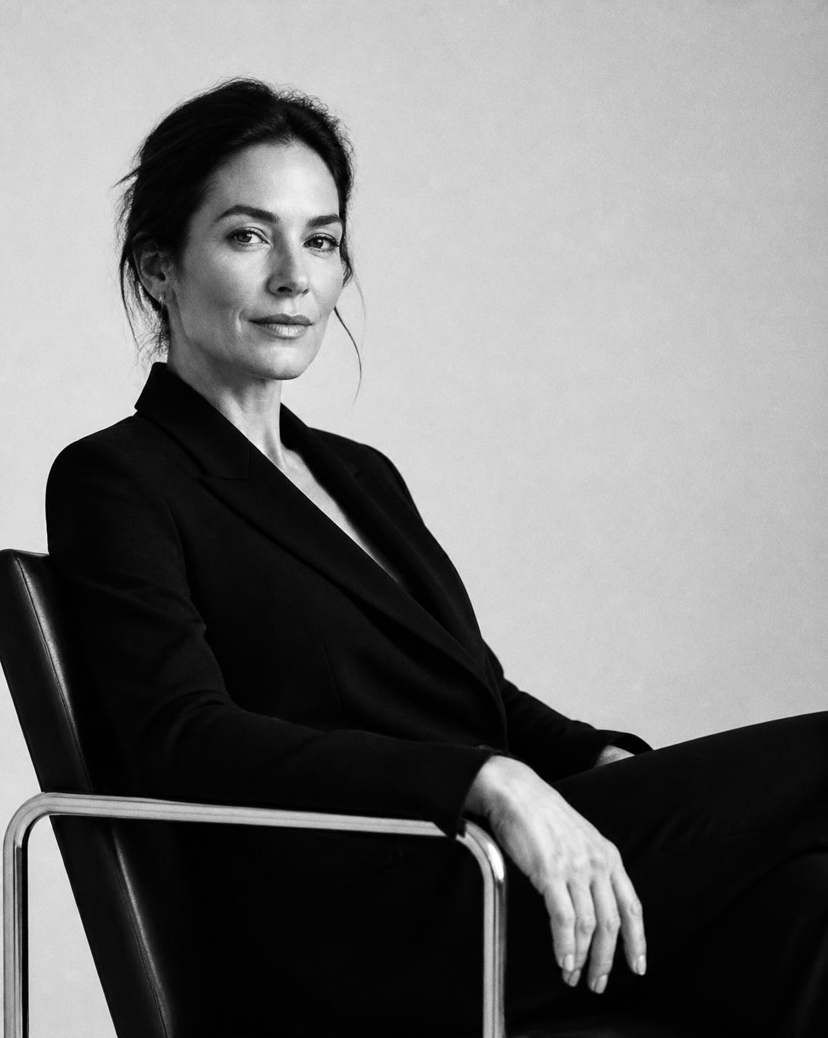 A woman in a tailored blazer seated in a modern chair
